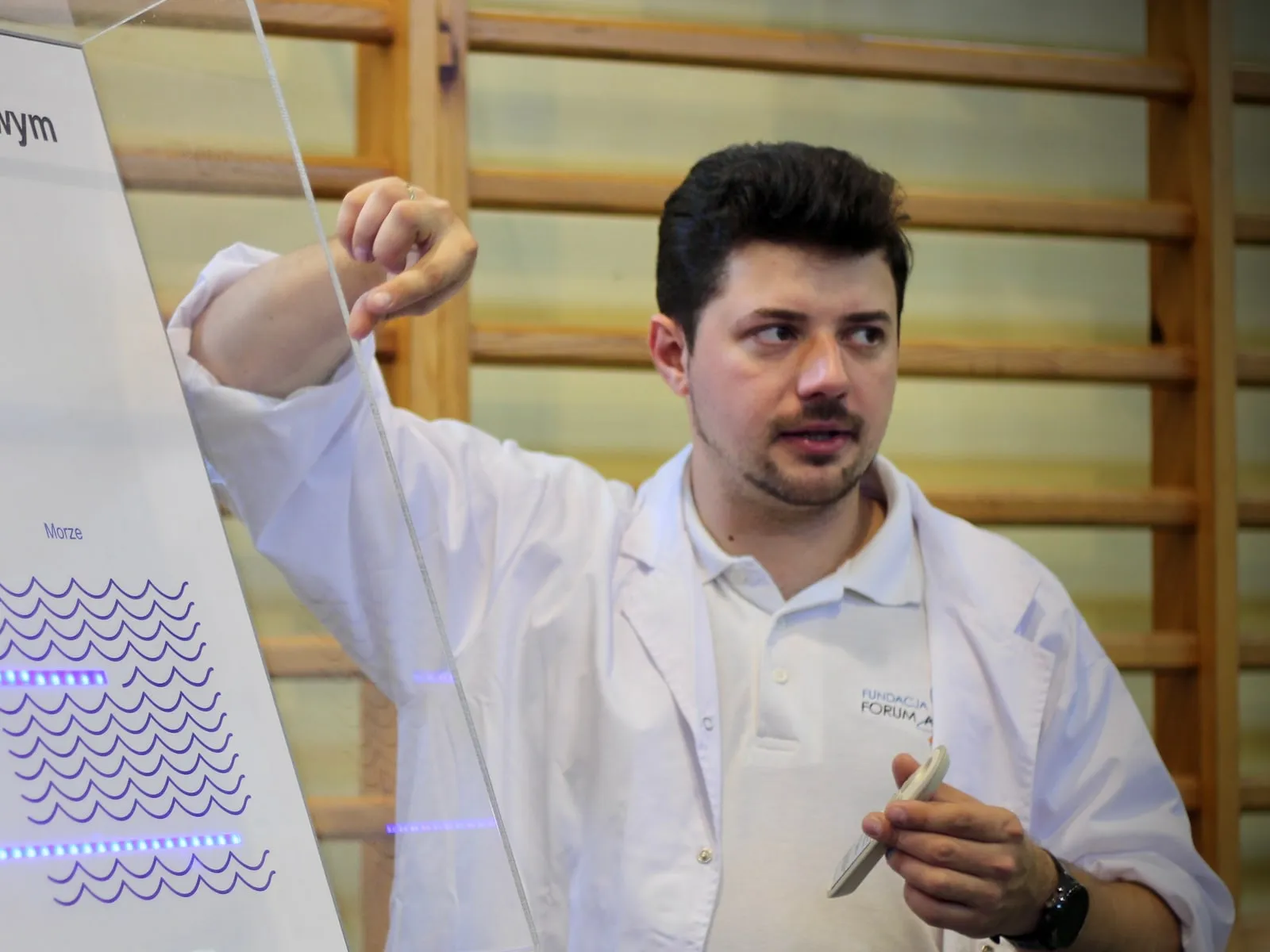 Osoba z zespołu Fundacji w fartuchu laboratoryjnym objaśnia podświetlaną makietę elektrowni jądrowej z reaktorem wodno-ciśnieniowym